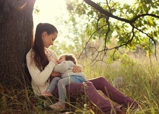 Junge Mutter stillt ihre vierjährige Tochter im Freien unter einem Baum