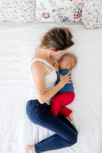 Mutter stillt Baby im Bett mit hochgezogenen Beinen und angewinkelten Armen.