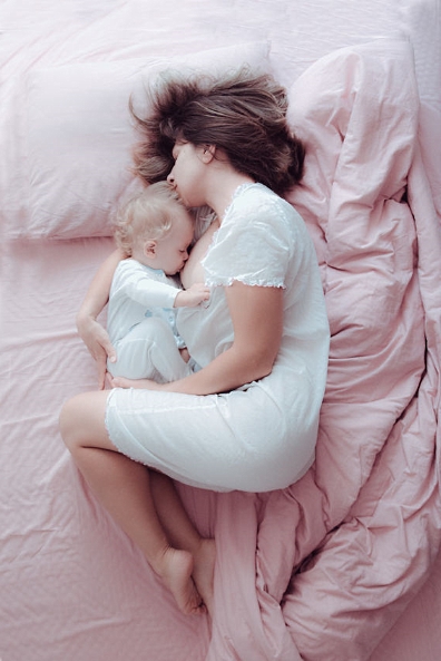 Mutter liegt im Bett mit Baby und umhüllt seinen ganzen Körper mit ihrem eigenen Körper.
